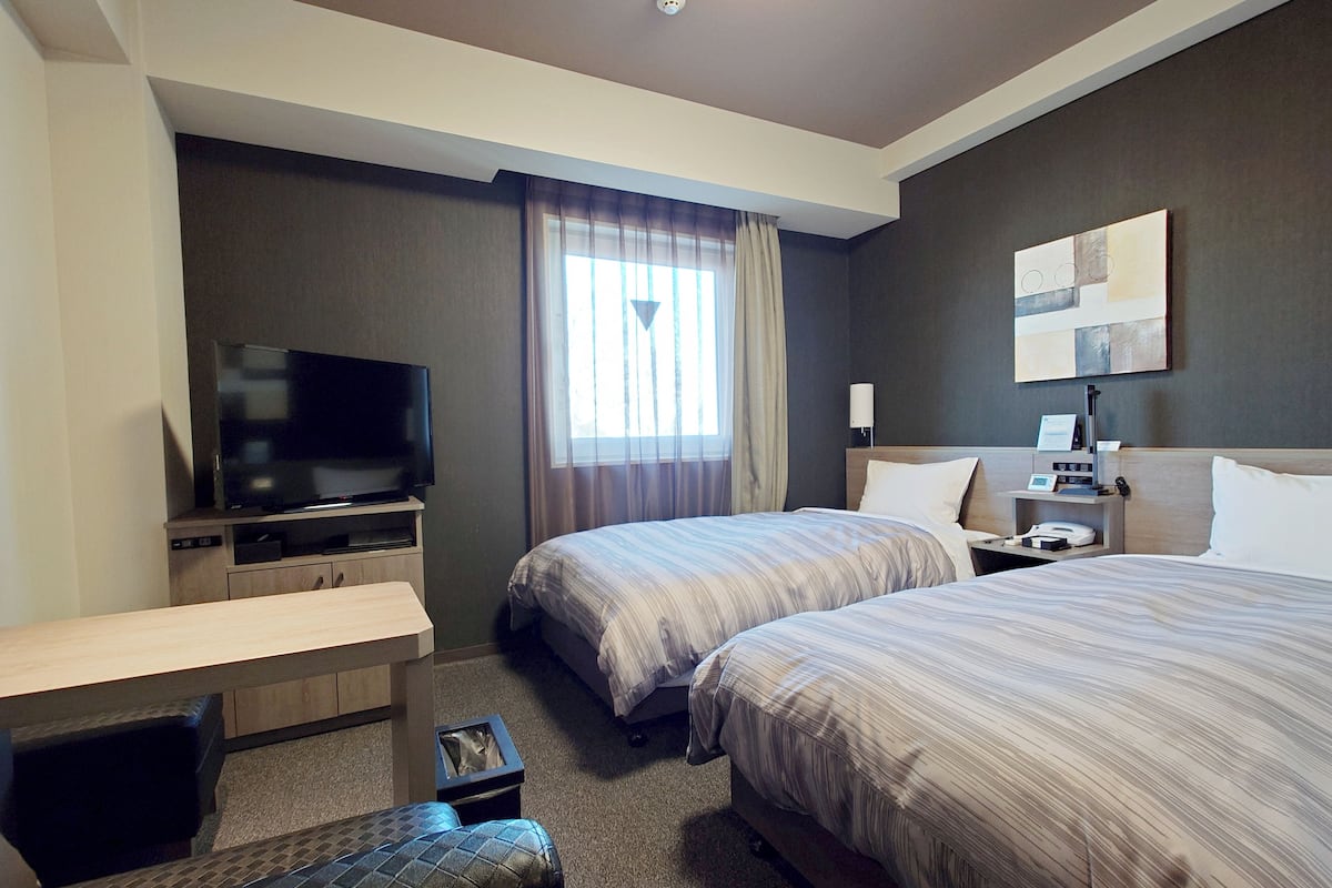 A hotel room with two beds, a TV, a desk, and a small table.