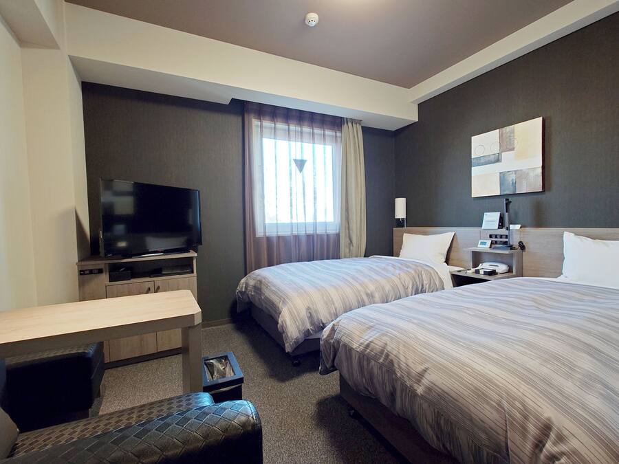 Habitación de hotel con dos camas, televisión, escritorio y una mesita.