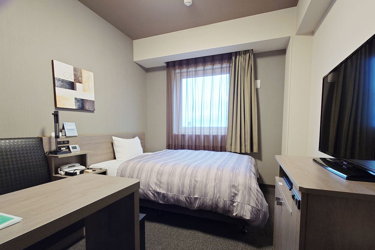A hotel room with a bed, desk, chair, television, and a window with curtains.