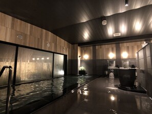 Un espace piscine intérieur moderne, doté d’un mur en verre, de lambris en bois et d’un élément décoratif central avec de l’eau.