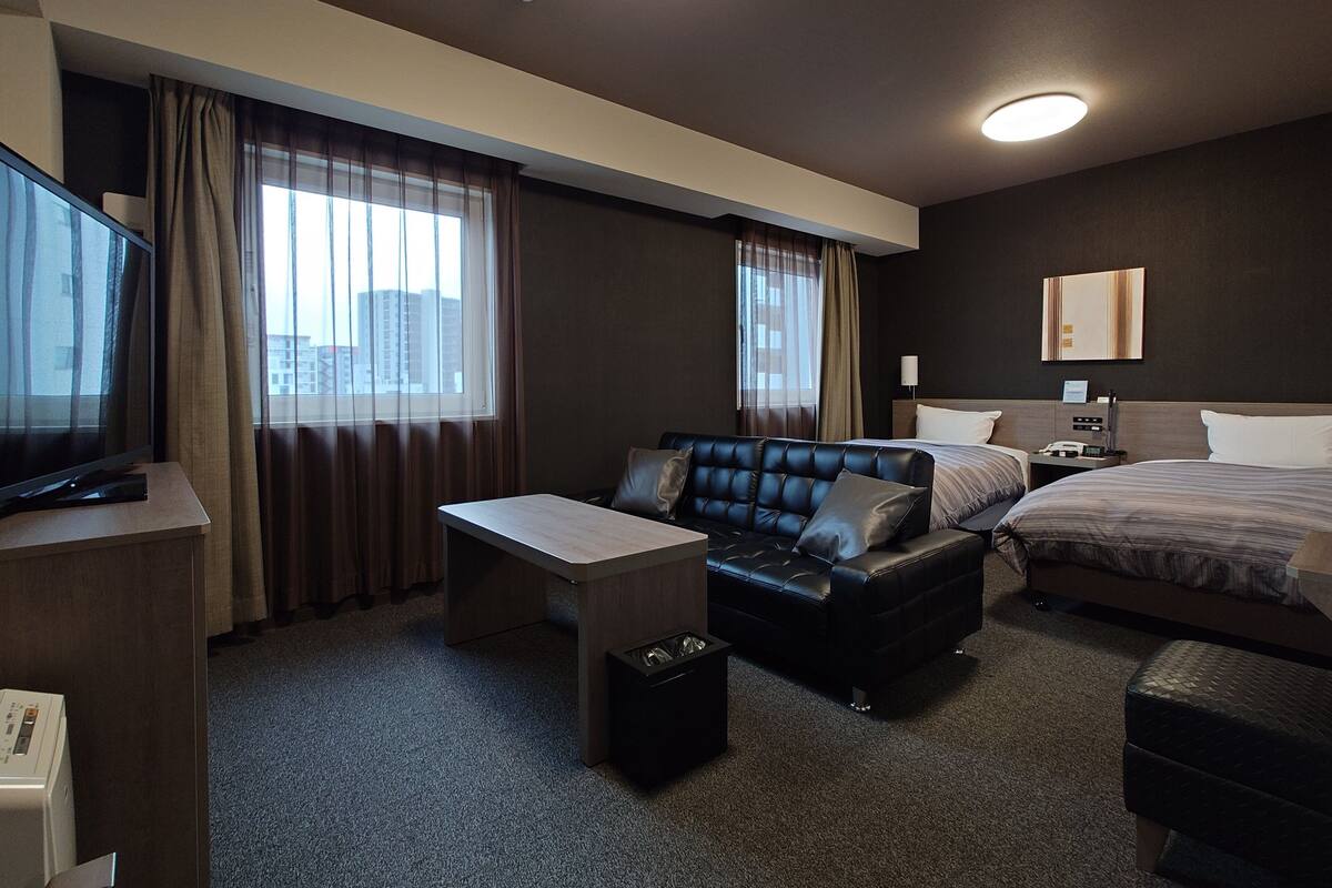 A hotel room with a bed, a sofa, a desk, and a television.
