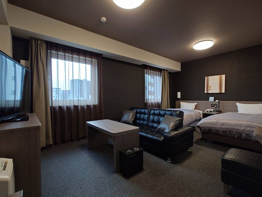 A hotel room with a bed, a sofa, a desk, and a television.