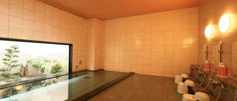 A modern bathroom with a glass-enclosed shower, multiple sinks, and a view of indoor plants.