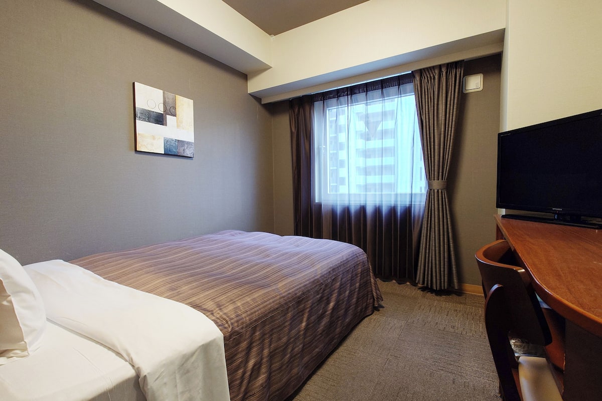 A hotel room with a bed, a desk, a television, and a window with curtains.