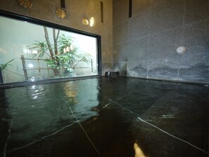 Un espacio interior amplio con piso pulido, un ventanal con vista a plantas, y una pared con un reloj y placas decorativas.