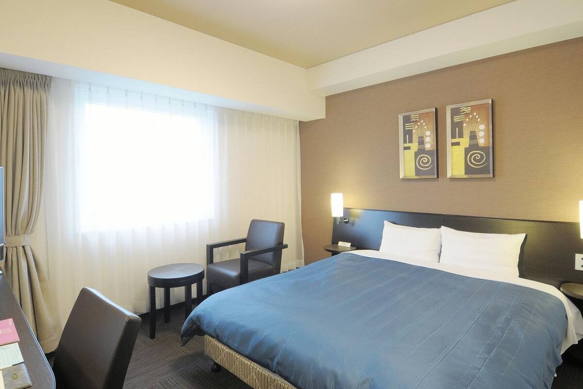 Habitación de hotel con una cama grande, un escritorio, una silla y dos lámparas de pared.