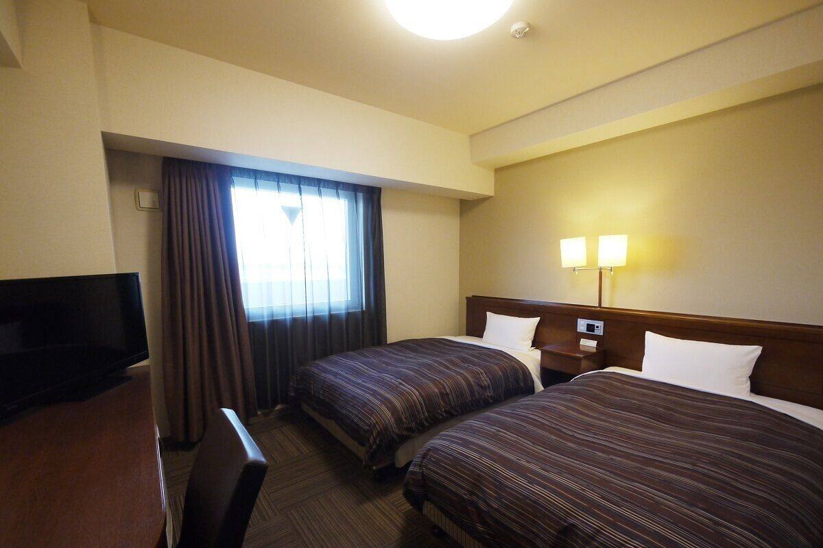 Una habitación de hotel con dos camas, televisión, escritorio y lámpara.