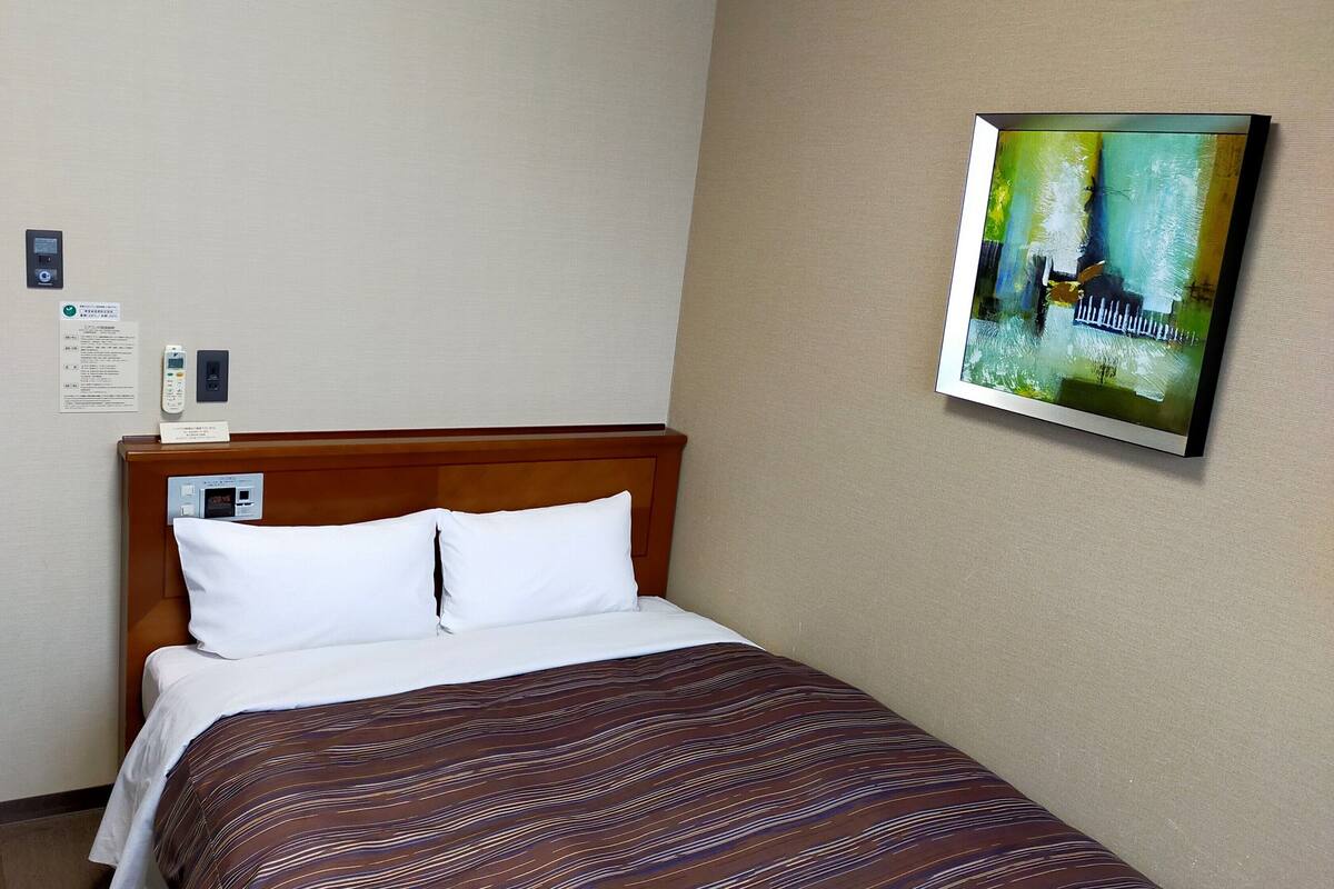 Una habitación de hotel con una cama, un cuadro colgado en la pared, una mesita de noche y una puerta con un letrero.