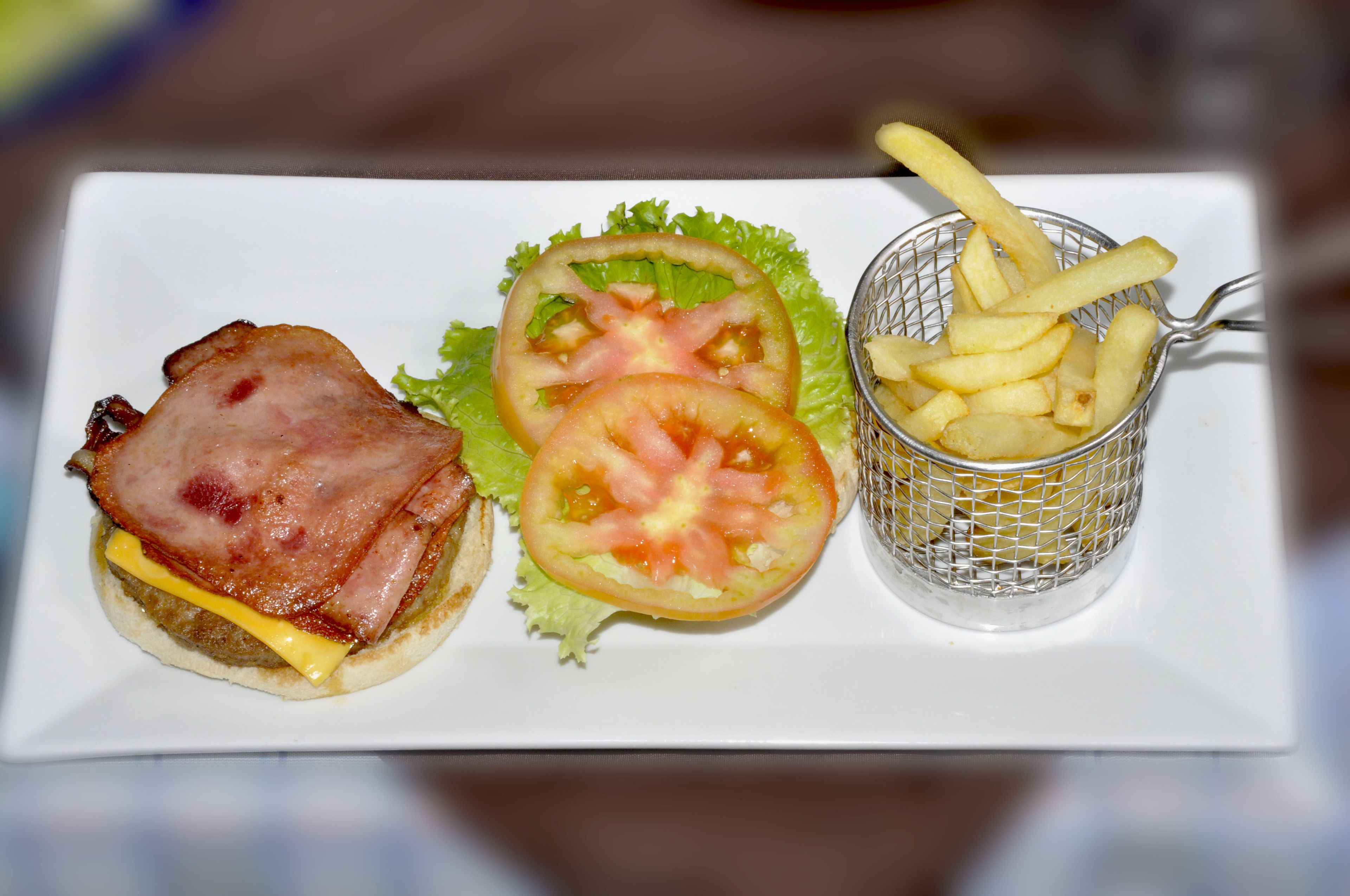 A sandwich with bacon, cheese, and lettuce, accompanied by a side of French fries and a tomato slice on a white plate.