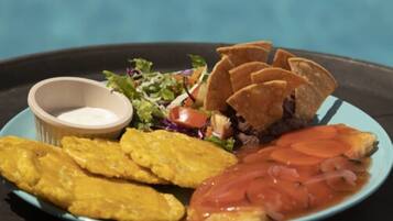 Une assiette contenant des bananes plantains frites, une salade, une tranche de viande, des chips de tortillas et une sauce pour tremper.
