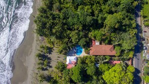 An aerial view of a coastal property with a swimming pool, surrounded by dense tropical vegetation and a beach. - Hotel Playa Westfalia (Matama)