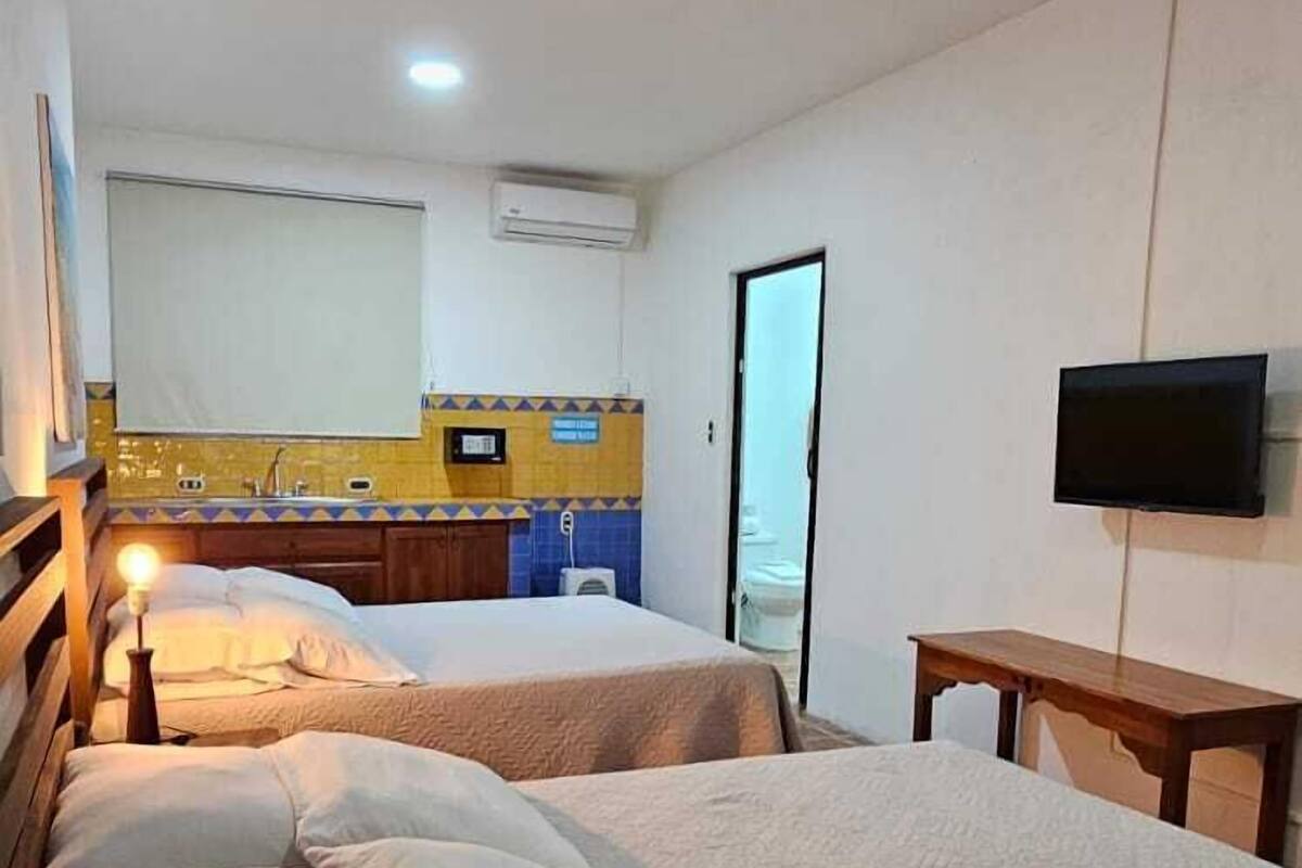 A hotel room with two beds, a small kitchenette, a TV, and an air conditioning unit.