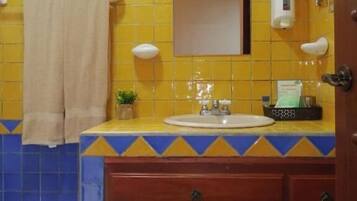 Un bagno con piastrelle gialle e blu, un lavandino con uno specchio sopra, un asciugamano appeso al muro e un dispenser di sapone.