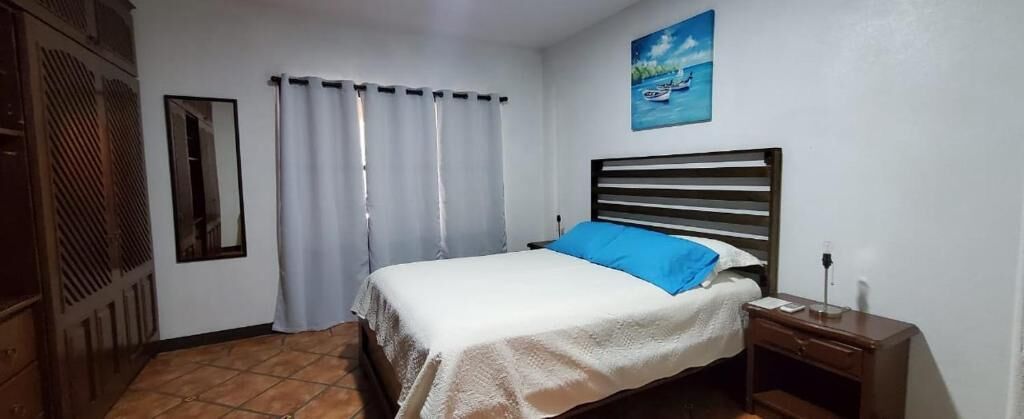 A bedroom with a bed, a nightstand, a mirror, and a painting on the wall.