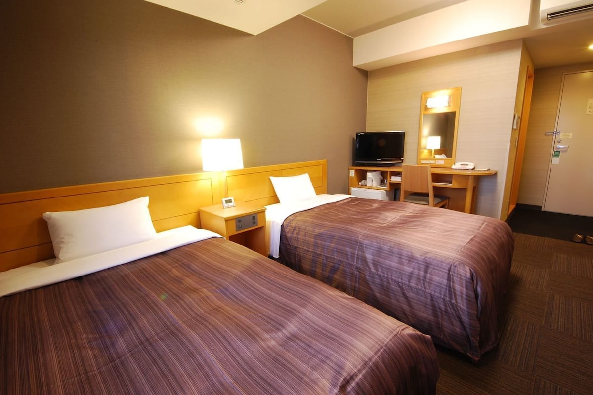 Une chambre d’hôtel avec deux lits, une télévision, un bureau et un miroir.