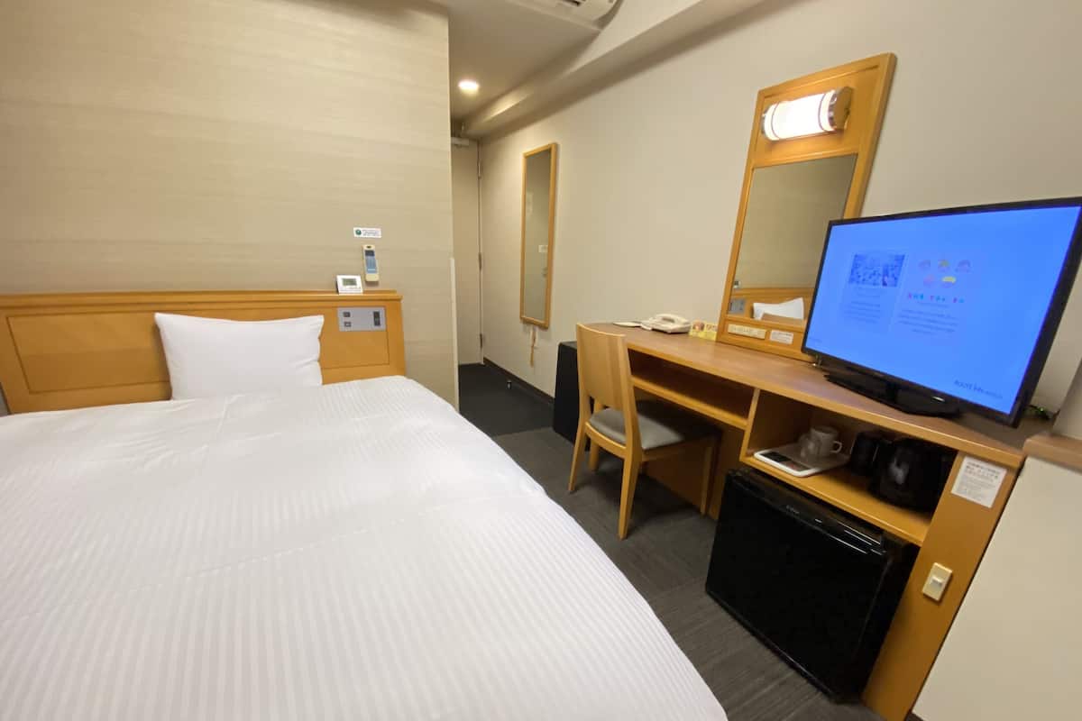 Une chambre d’hôtel équipée d’un lit, d’un bureau, d’une chaise, d’une télévision et d’un petit réfrigérateur.