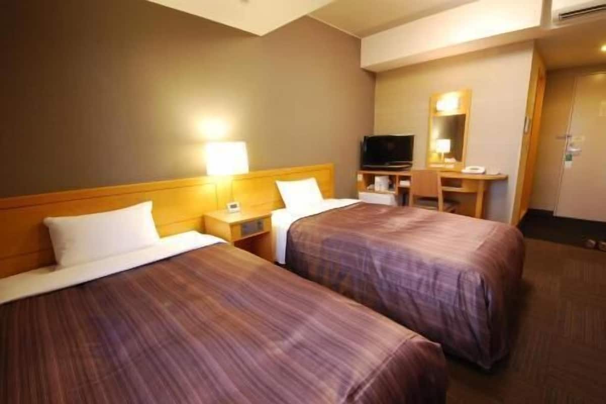 Une chambre d’hôtel avec deux lits, un bureau, une télévision et un miroir.