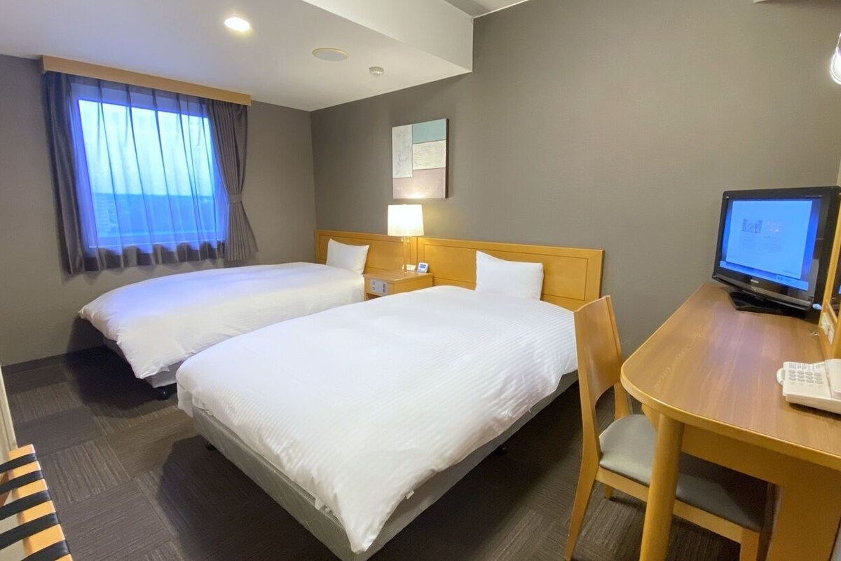 A hotel room with two beds, a desk with a computer, and a window with curtains.