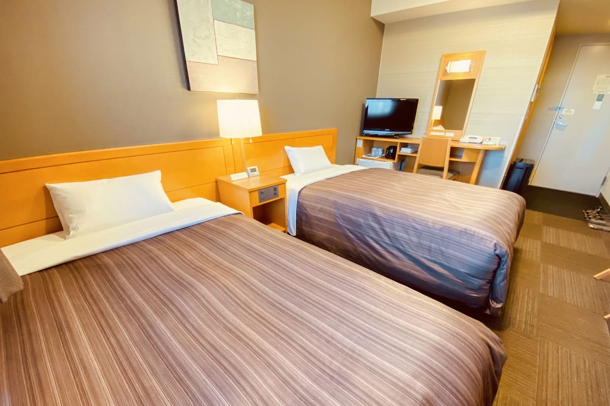 Une chambre d’hôtel avec deux lits, une télévision, un bureau et un miroir.