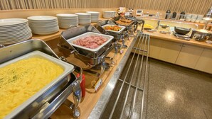Un aparador de buffet amb diversos aliments en plats metàl·lics, piles de plats i una paret de fusta amb línies verticals.