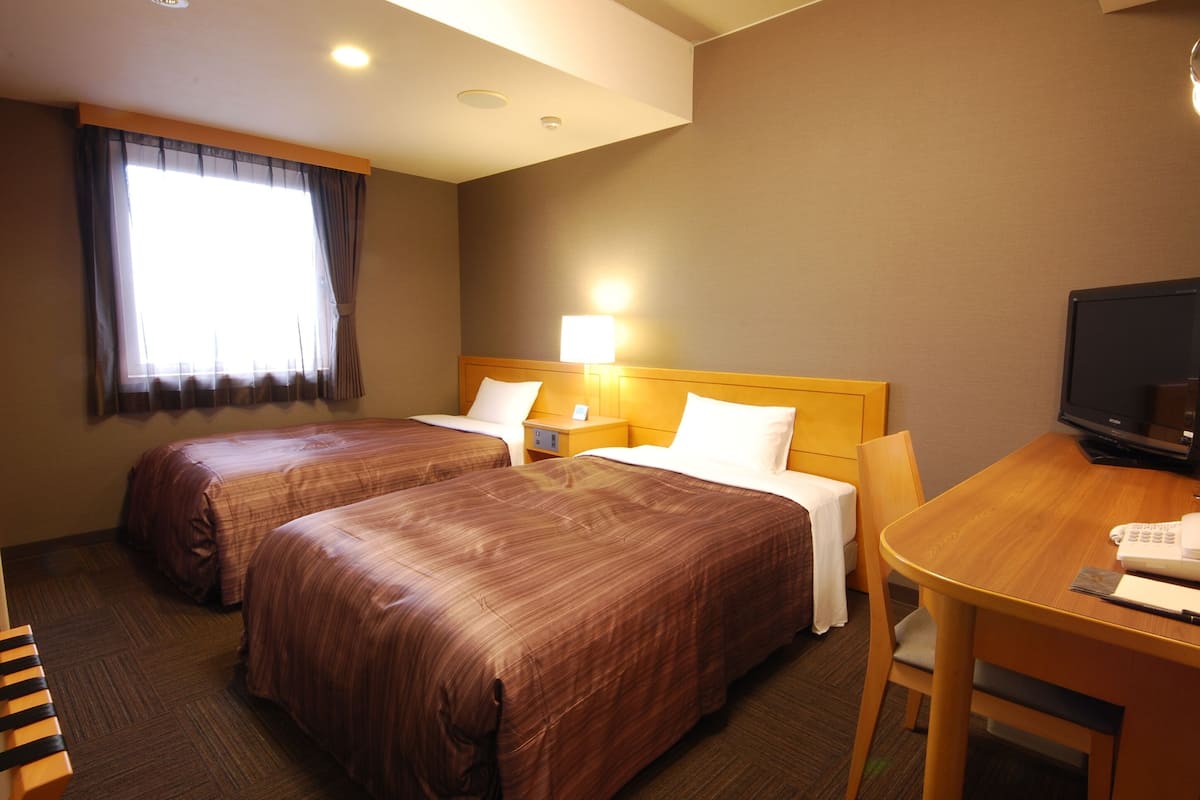 Une chambre d’hôtel avec deux lits, un bureau, une chaise, une télévision et une lampe.