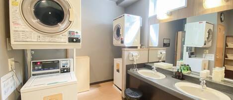A hotel bathroom with a washing machine, dryer, and a sink with a mirror.