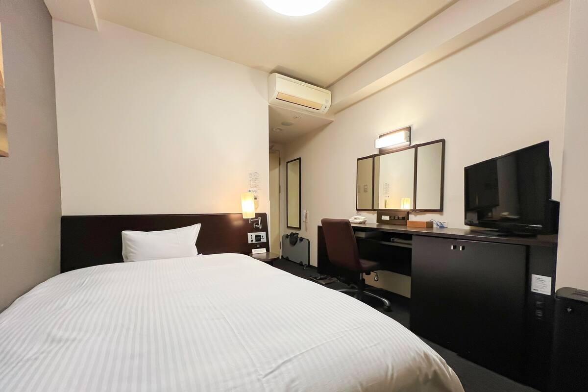 A hotel room with a large bed, a desk with a chair, a television, and a mirror.