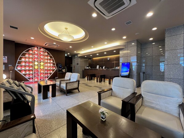 A modern hotel lobby with seating areas, a reception desk, and a digital screen.