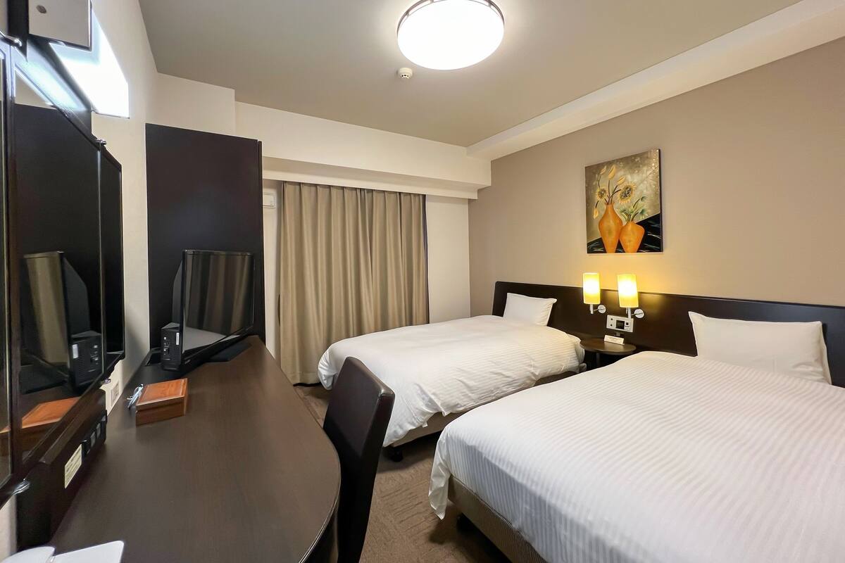 A hotel room with two beds, a desk with a computer, a mirror, and a painting on the wall.