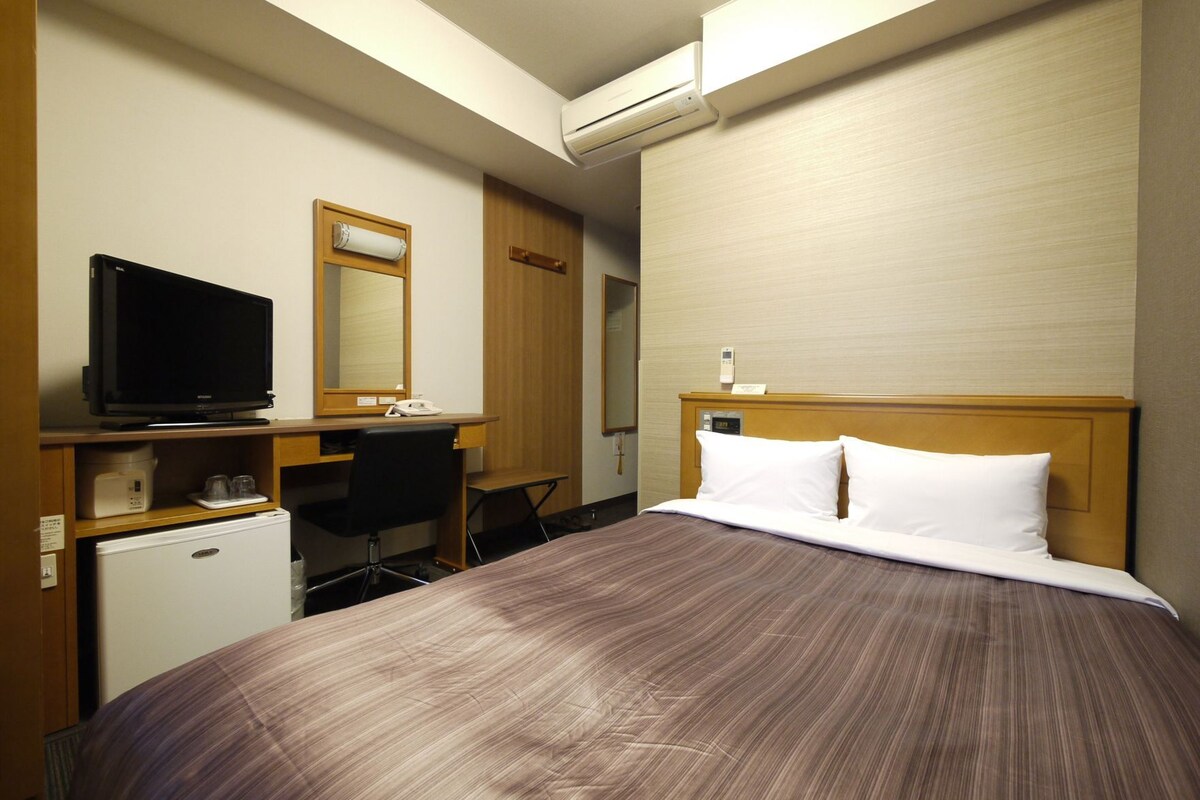 A hotel room with a bed, a desk with a computer, a television, and a refrigerator.