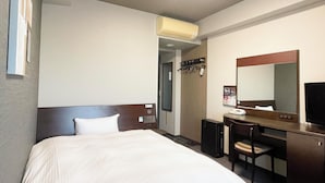Habitación de hotel con cama, escritorio, silla, espejo y aire acondicionado instalado en la pared.