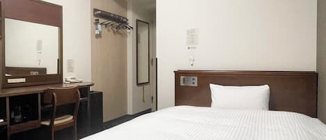 Una camera d'albergo con un letto, una scrivania con una sedia, uno specchio, un condizionatore d'aria e un appendiabiti.