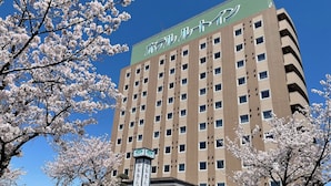 Un hotel de varios pisos con un letrero verde, rodeado de cerezos en flor.