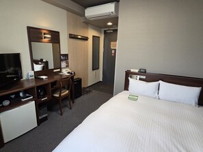 A hotel room with a bed, a desk with a chair, a television, a mini-fridge, a mirror, and an air conditioning unit. - Hotel Route-Inn Odate Eki Minami (Odate)