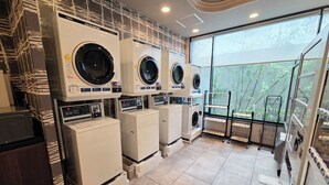 A laundry room with multiple washing machines and dryers, a tiled floor, and a view of bamboo outside. - Hotel Route-Inn Odate Eki Minami (Odate)