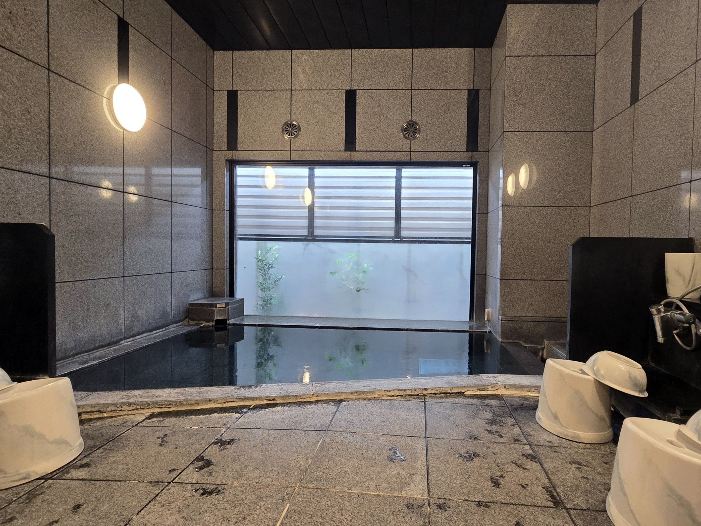 Un baño moderno con una bañera grande, una ventana con persianas y una pared de piedra.