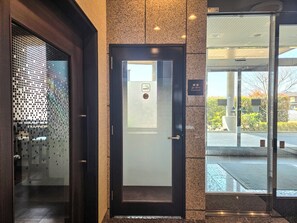 Entrada de un hotel con puerta de vidrio, un letrero que indica zona para fumadores y vista de la calle.
