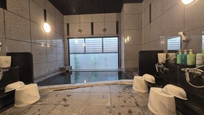 Un baño moderno con un espejo grande, un lavabo negro y una zona de ducha con mampara de vidrio.