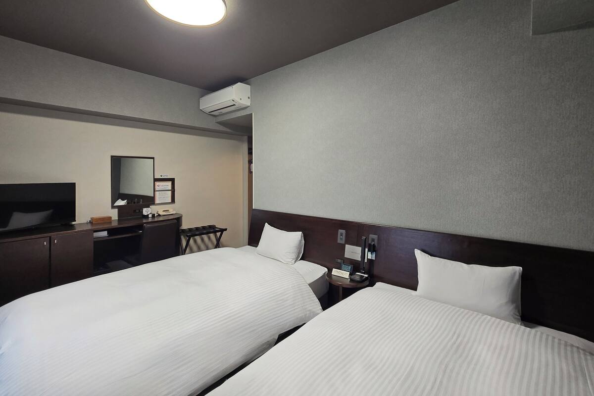 Una habitació d'hotel amb dos llits, un escriptori amb televisió de pantalla plana, un mirall i un aparell d'aire condicionat a la paret.