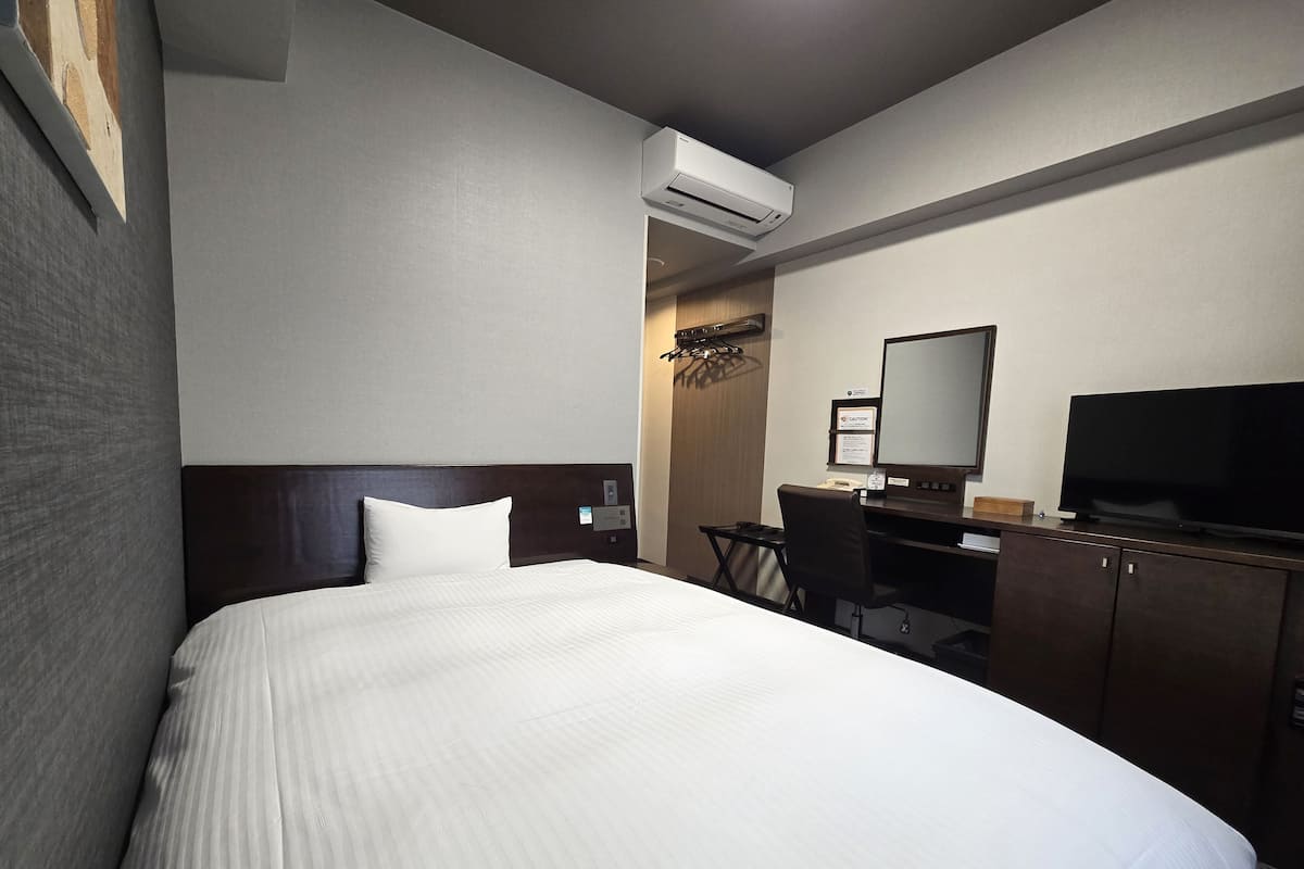 Una habitació d'hotel amb llit, escriptori, cadira, televisió i aire condicionat.