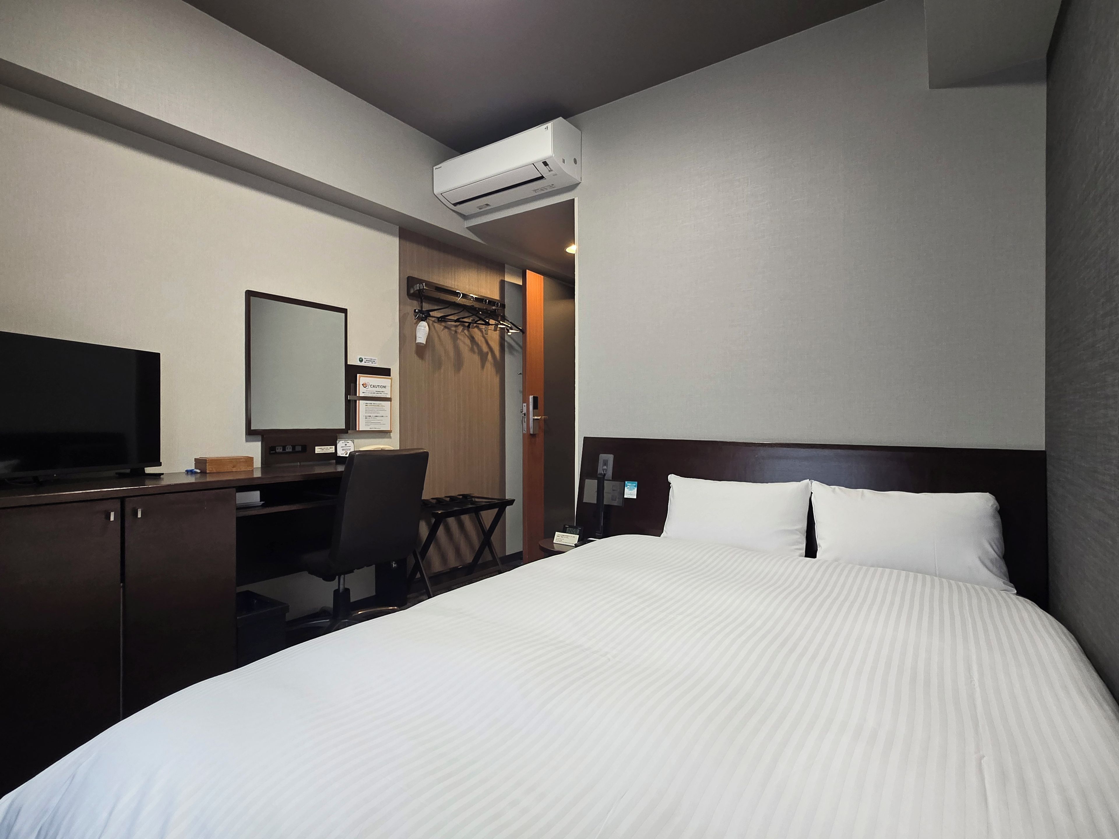 Habitación de hotel con cama, escritorio, computadora, televisor y aire acondicionado.