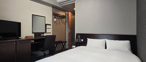 A hotel room with a bed, a desk with a computer, a television, and an air conditioning unit.