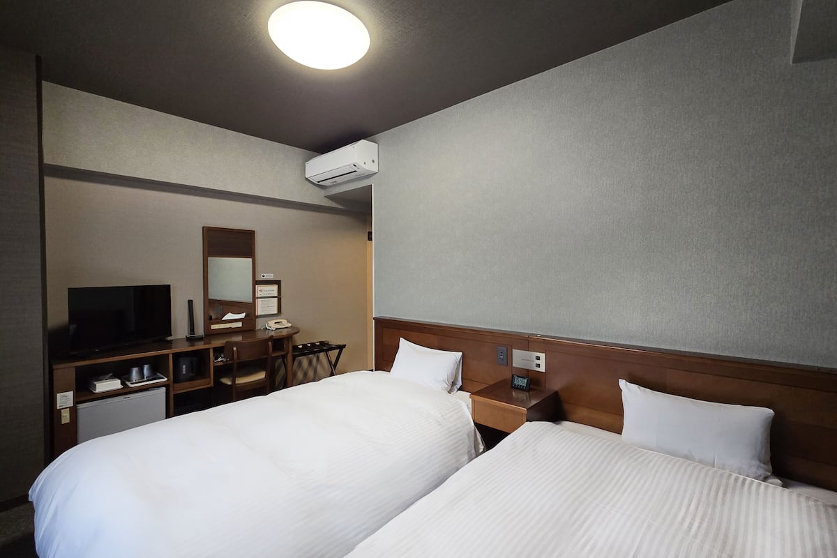 Habitació d'hotel amb dos llits, un escriptori amb cadira, una televisió i un aire condicionat.