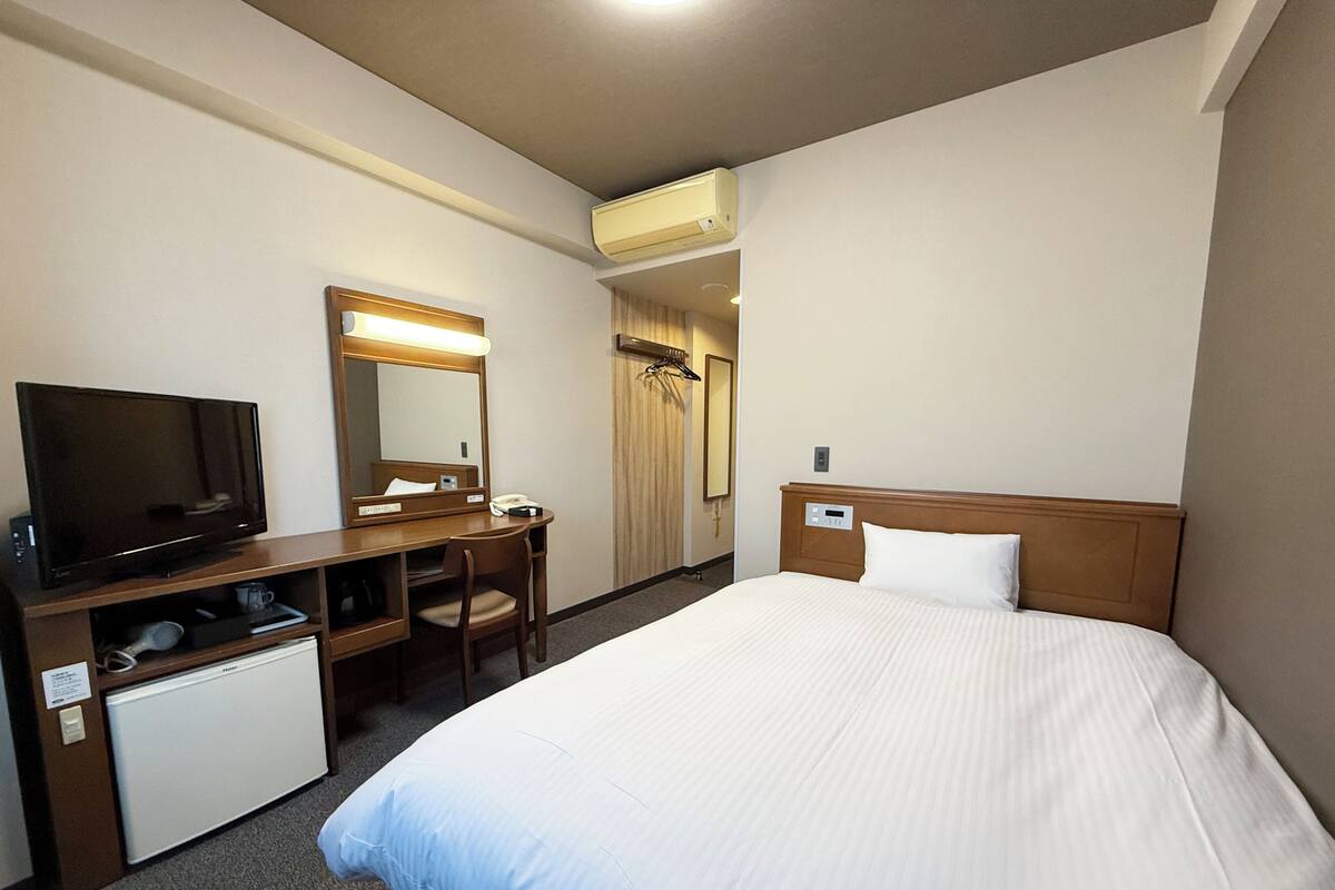 A hotel room with a bed, a desk with a television, a mirror, and a wardrobe.