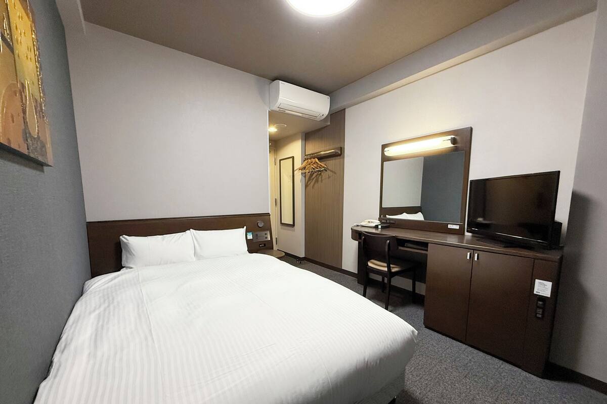 A hotel room with a large bed, a desk with a chair, a television, and a mirror.