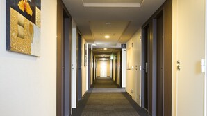 Un largo y estrecho pasillo de hotel con pisos alfombrados, puertas a ambos lados y una lámpara en el techo.