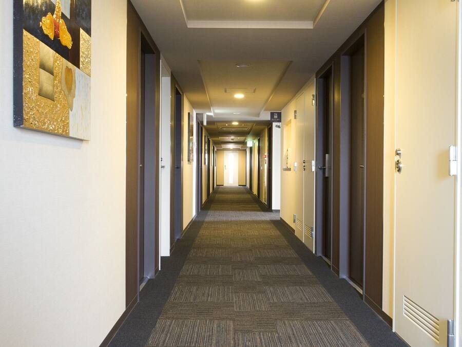 Un largo y estrecho pasillo de hotel con pisos alfombrados, puertas a ambos lados y una lámpara en el techo.