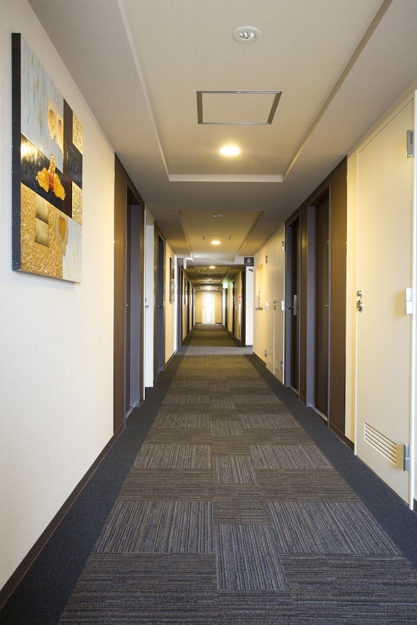 A long, narrow hotel corridor with carpeted floors, doors on both sides, and a ceiling light fixture.