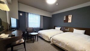 Habitación de hotel con dos camas, un escritorio con teléfono, una silla, una mesita y un televisor.