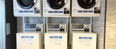 A row of three front-loading washing machines and three front-loading dryers, each with a digital display and control panel, in a commercial setting.